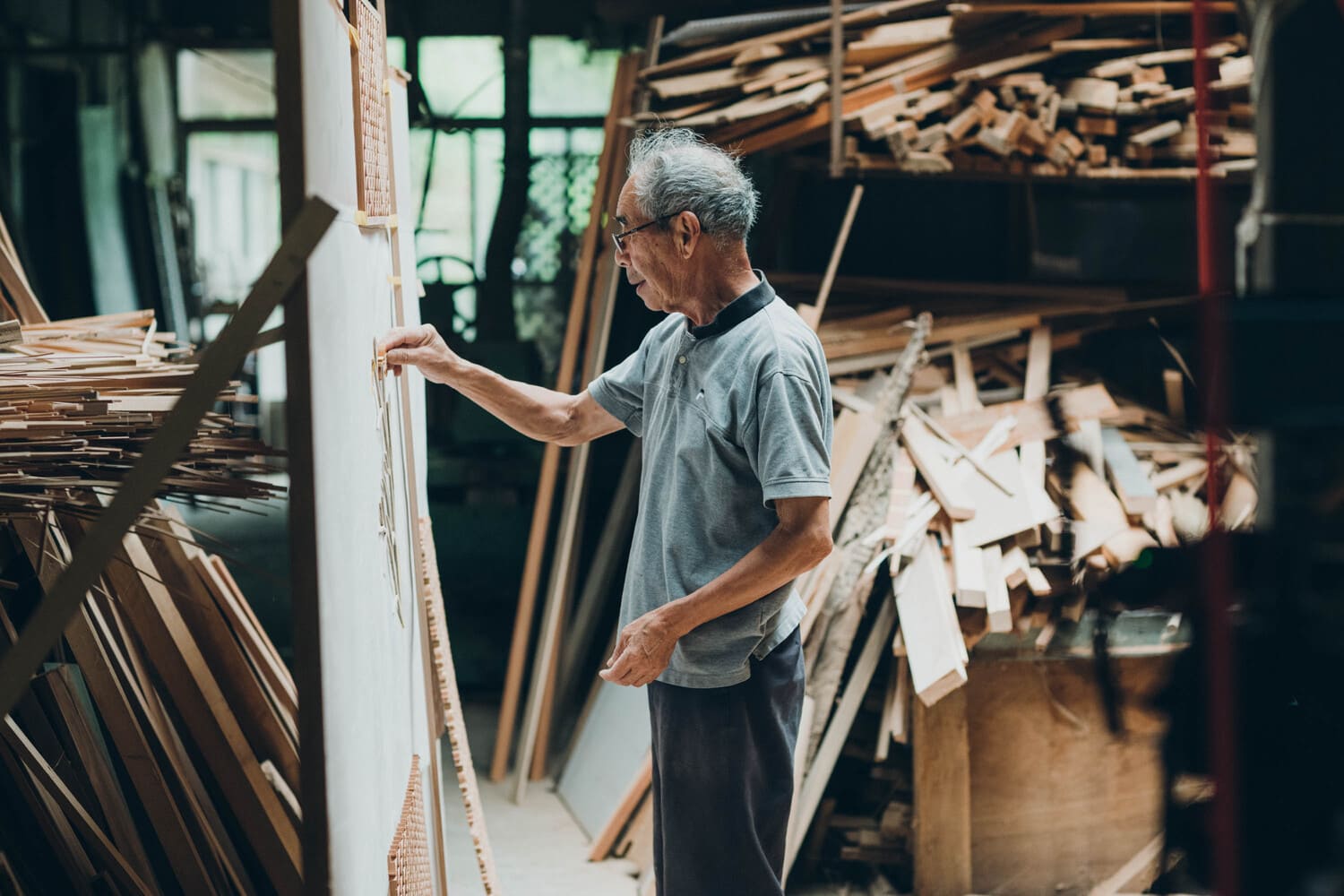 加工場で木材に囲まれながら作業する男性の写真